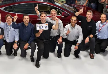 Tesla's executive team kneeling in front of a red Model S, one holding a TSLA S1 license plate